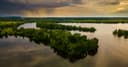 A lake with wooded islands seen from above at sunset, with rain clouds in the distance