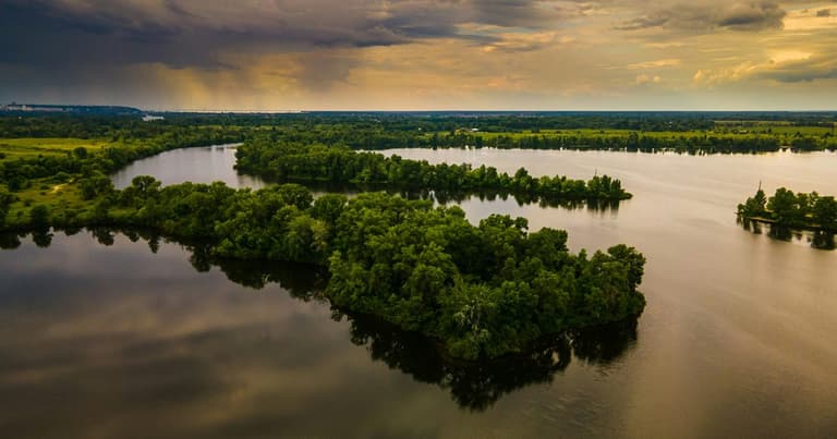 A lake with wooded islands seen from above at sunset, with rain clouds in the distance