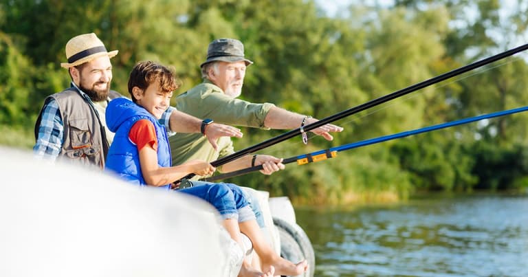A grandfather, a father and a boy fishing together from a jetty in summer