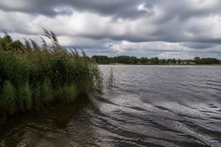 A carp lake under a broken sky, wind putting a ripple on the windward bank